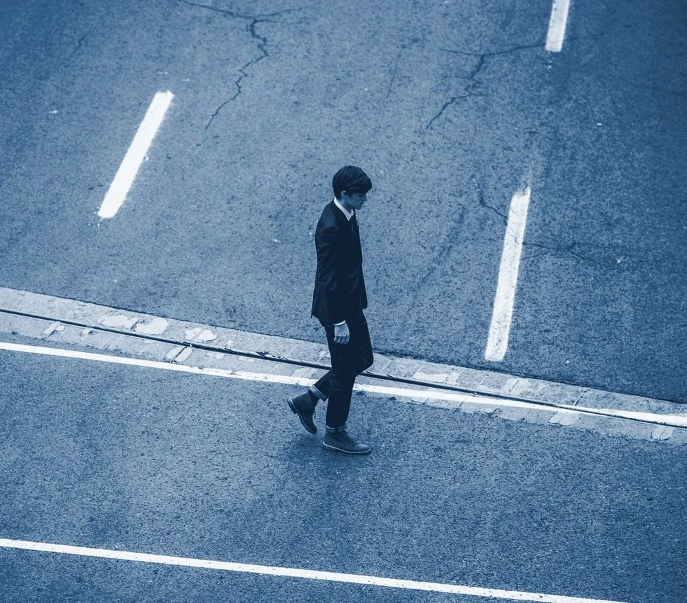 Aerial view of a single person in a suit crossing an empty, clearly marked road